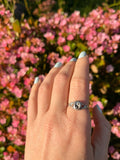 Woman's hand with silver yin yang ring and backdrop of pink flowers